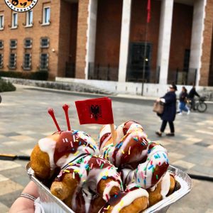 main tenant une barquette de beignets avec un petit drapeau albanais