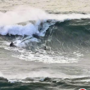 surfeur de l'extrême ridant une immense vague, accompagné d'un jet-ski