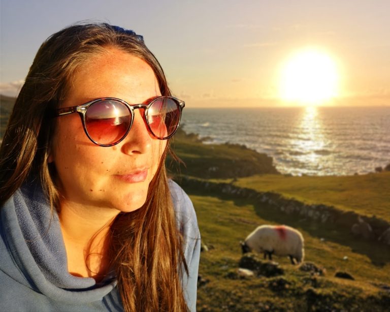 portrait d’Elisa, travel planner, avec le coucher de soleil se reflétant dans ses lunettes, la mer en arrière-plan