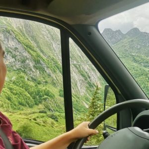 Elisa, Travel Planner, au volant de son van lors d'un road trip dans les montagnes verdoyantes des Hautes-Pyrénées françaises
