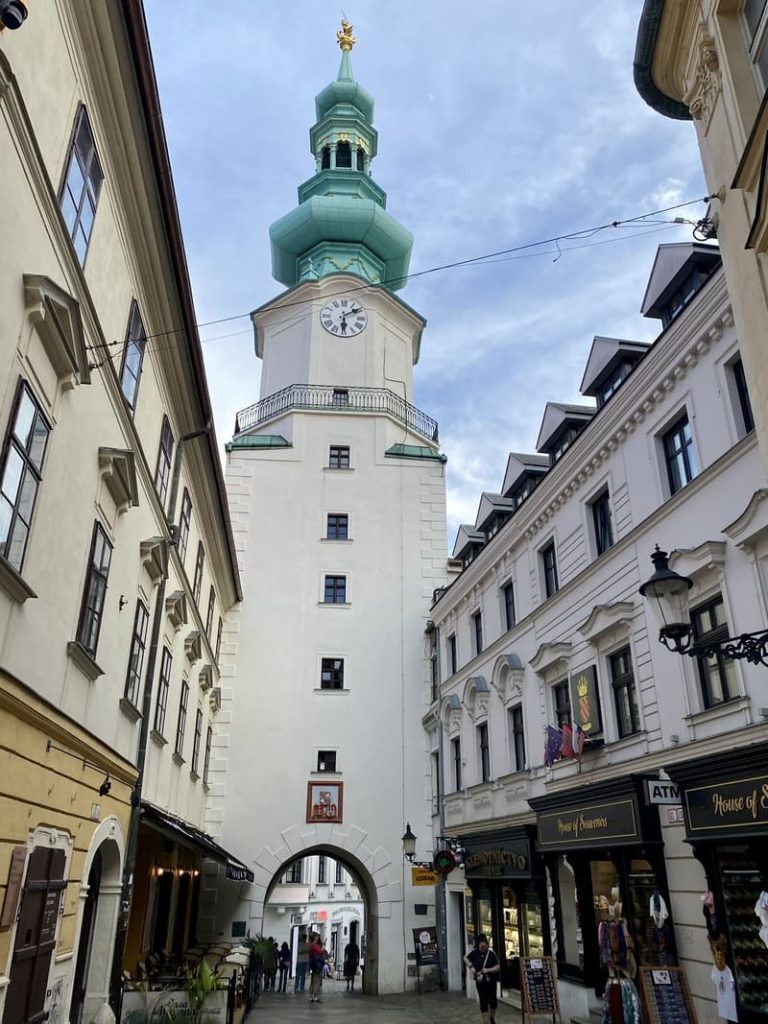 La Porte Saint-Michel avec sa tour blanche et son dôme vert surplombant une rue piétonne de Bratislava.