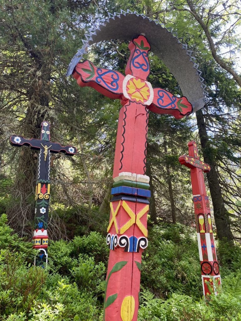 Grandes croix de Detva en bois sculptées et colorées, dressées au milieu de la végétation.