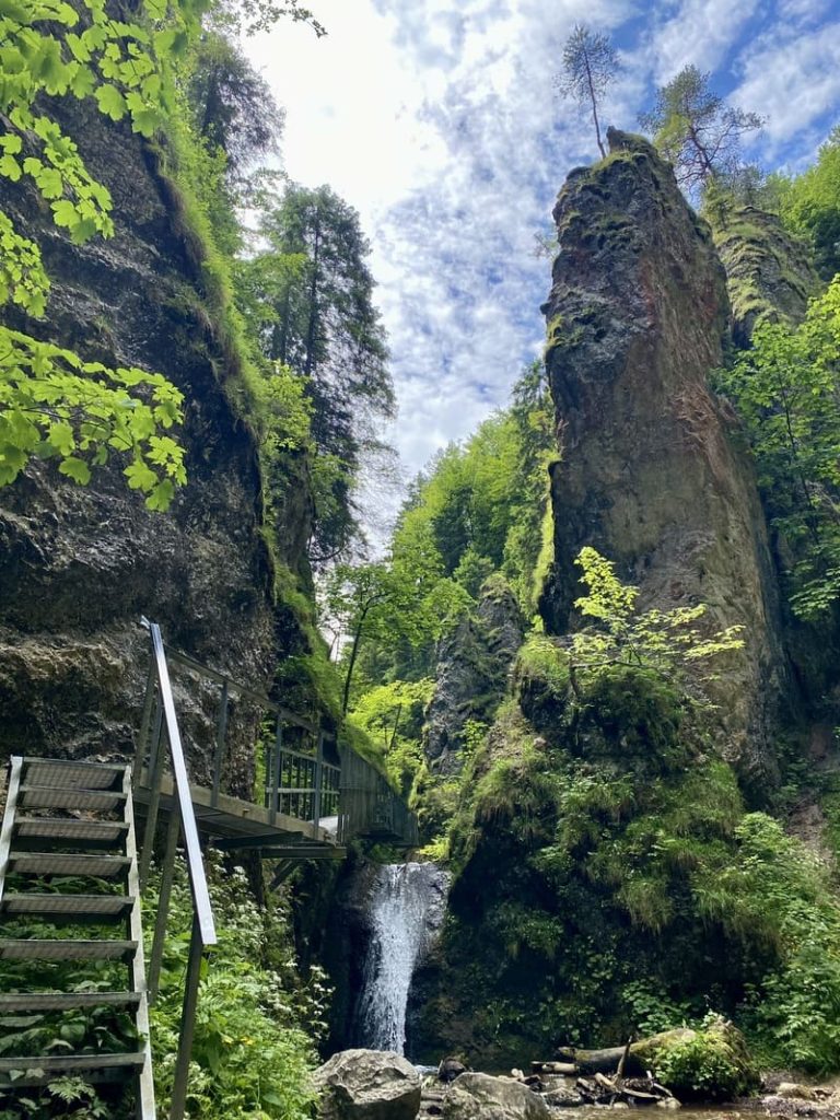 Une cascade coulant entre de hautes falaises rocheuses verdoyantes avec une passerelle métallique dans la Malá Fatra.